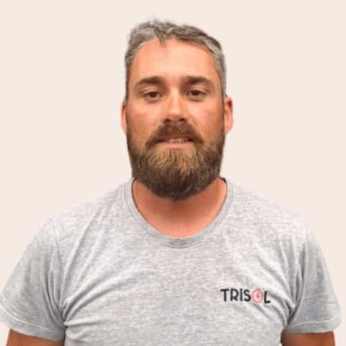 Portrait of a man with gray hair and a full beard, wearing a light gray TRISOL t-shirt and looking at the camera. | Notre équipe | Notre équipe