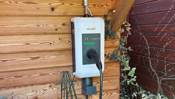 Wall-mounted EV charging station with a plugged-in charging cable mounted on a wooden wall.