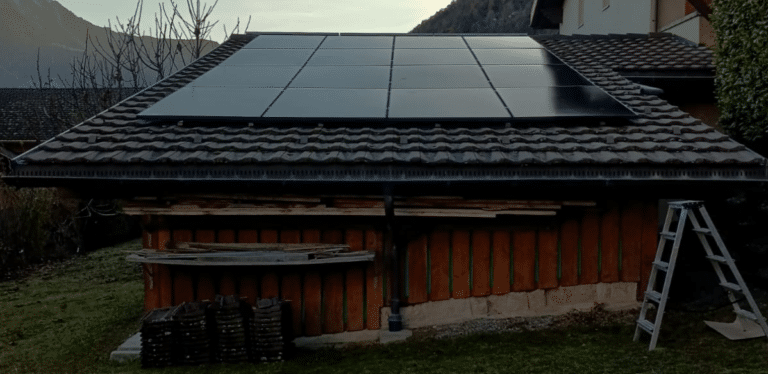 Rooftop solar panels installed on a low-tiled roof with a ladder and building materials in the yard. | Extension solaire photovoltaïque à Chamoson | Nos réalisations