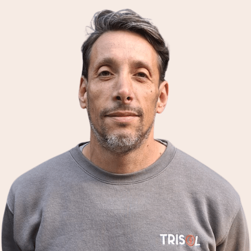 Portrait of a man with short dark hair and light stubble, wearing a gray crew-neck sweatshirt with a TRISOL logo on the chest, against a pale background. | Notre équipe | Notre équipe