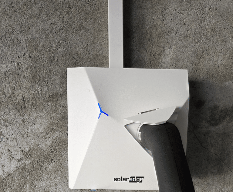 White SolarEdge inverter with angular design mounted on a rough concrete wall; blue indicator and black power cable visible. | Borne de recharge à Morges | Nos réalisations