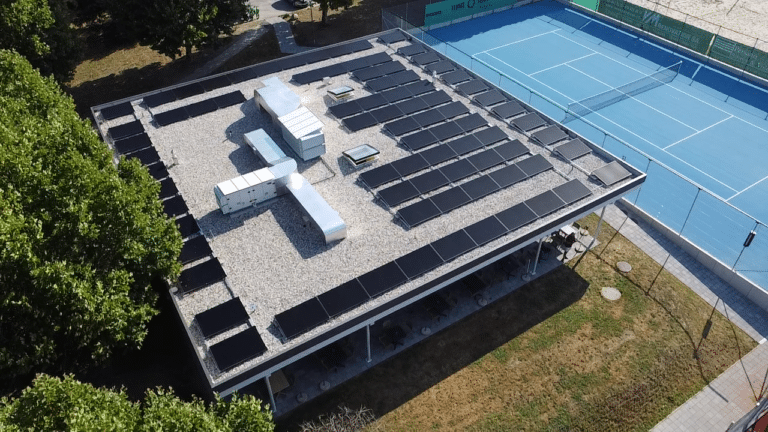 Flat rooftop covered with numerous solar panels beside a blue tennis court. | Installation photovoltaïque au Tennis Club d’Ecublens | Nos réalisations