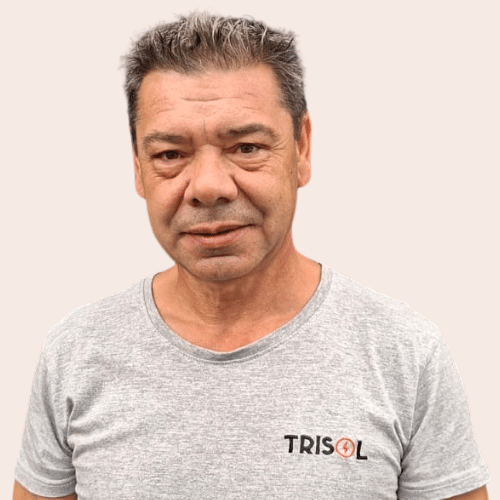 Portrait of a middle-aged man with short gray-streaked hair wearing a light gray TRISOL T-shirt against a beige background, with a neutral expression. | Notre équipe | Notre équipe